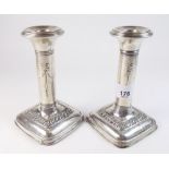 A pair of silver candlesticks embossed ribbon and decoration on weighted square bases - 14cm high