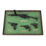 Four mounted miniature firearms: Sten; Beretta; Nagant; Nambu