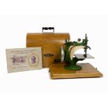 A wooden cased child's Grain manual sewing machine, green cast iron G frame on wooden base. Together