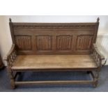 An early 20th Century oak settle, four linenfold panels to back, turned naturalistic supports united