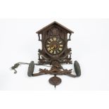 A black forest style cuckoo clock, featuring a chalet above some foliage, Arabic numeral with carved