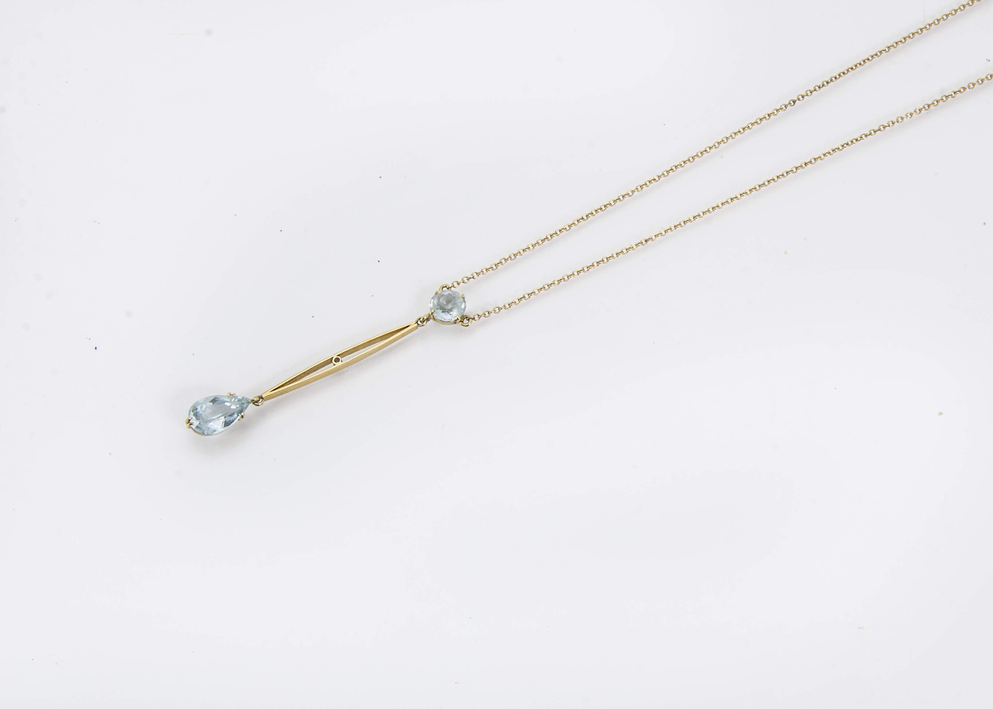 An Edwardian 15ct gold and aquamarine necklace, the chain supporting a round cut light blue stone