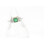 An Edwardian period three stone emerald and diamond ring, the central square cut emerald flanked