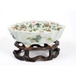 A Chinese canton glazed bowl, decorated with flowers and butterflies, placed upon a carved wooden