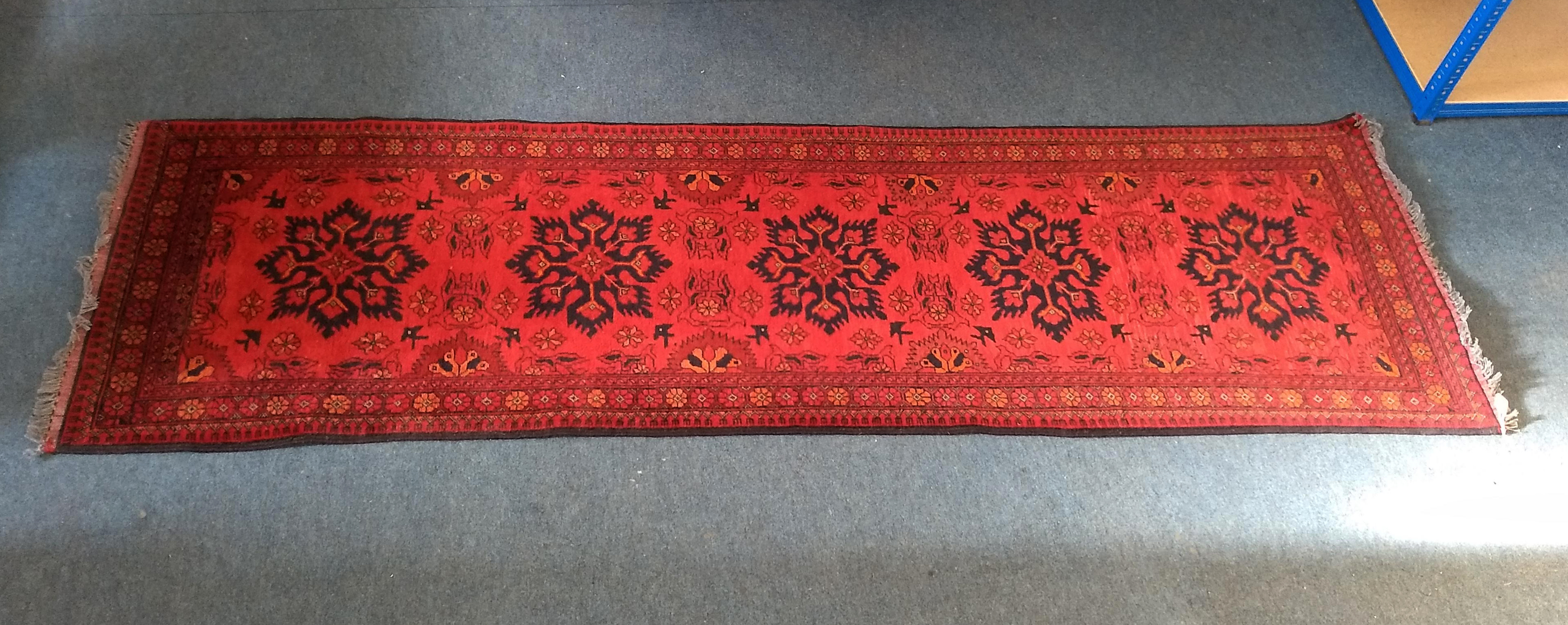 A woollen runner, single row of five motifs on red ground, within a rosette border, 85 cm x 285 cm