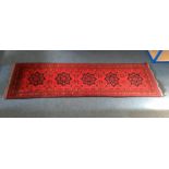 A woollen runner, single row of five motifs on red ground, within a rosette border, 85 cm x 285 cm