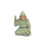 A Chinese celadon glazed stoneware model of a warrior, sitting cross-legged holding a lamp,