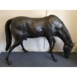 A contemporary bronzed garden sculpture of a horse lowering it's head to feed, 135 cm high x 194