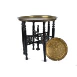A Middle-Eastern brass tray top table, on folding ebonised stand, circular tray with embossed