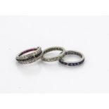 Three diamond, sapphire and ruby set eternity rings, comprising a full diamond example, ring size N,