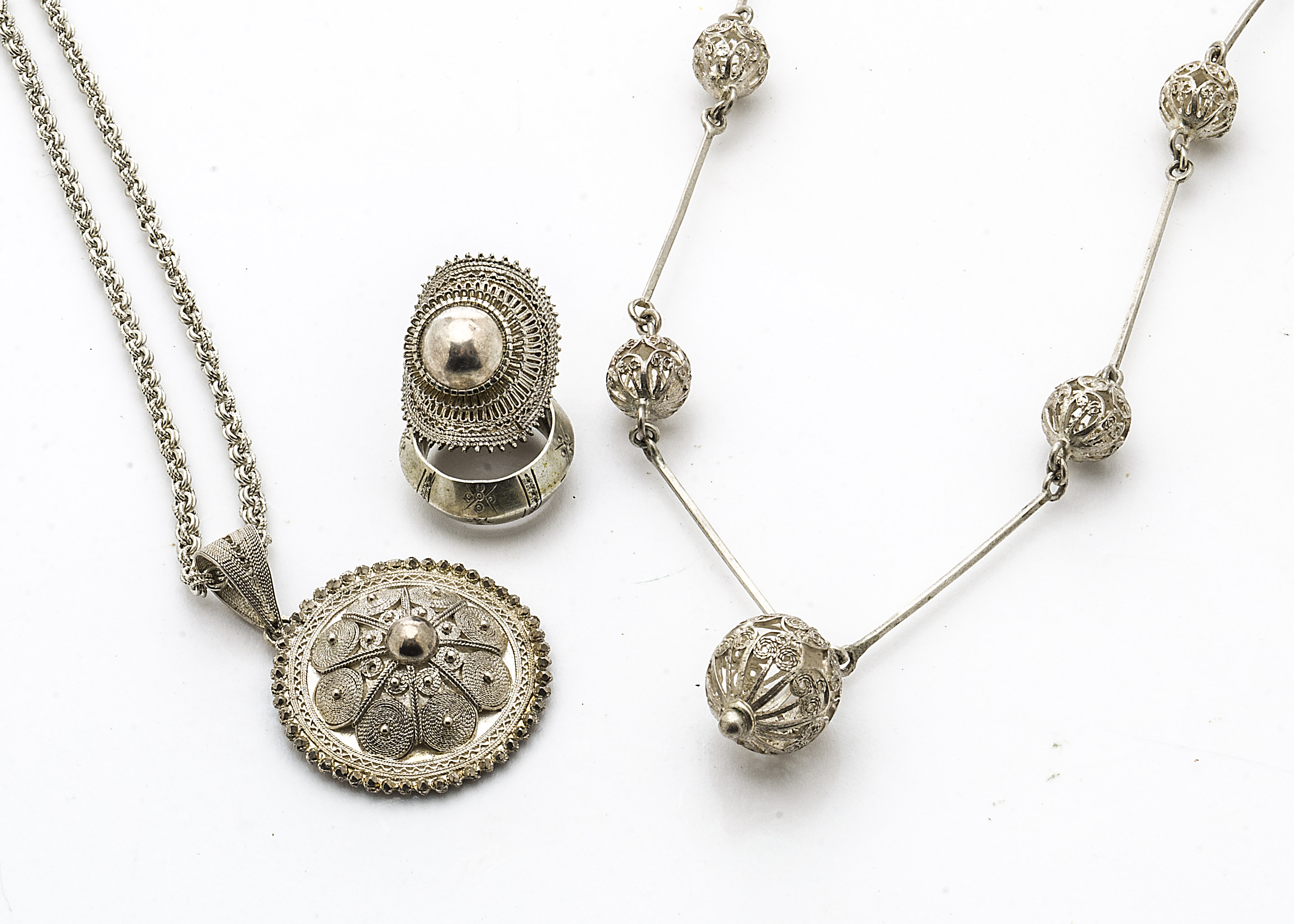 A collection of Ethiopian filigree white metal jewellery, including a roundel medallion, a sphere