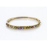 A continental yellow metal gem set bangle, the channel set square cut brown/pink gem stones in