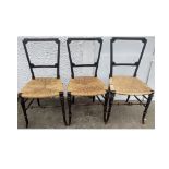 A set of three ebonised bedroom chairs, tapered backs, rush seats, turned supports, traces of