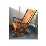 An Edwardian rocking chair, terracotta back rest, arms and seat, spring mechanism, castors