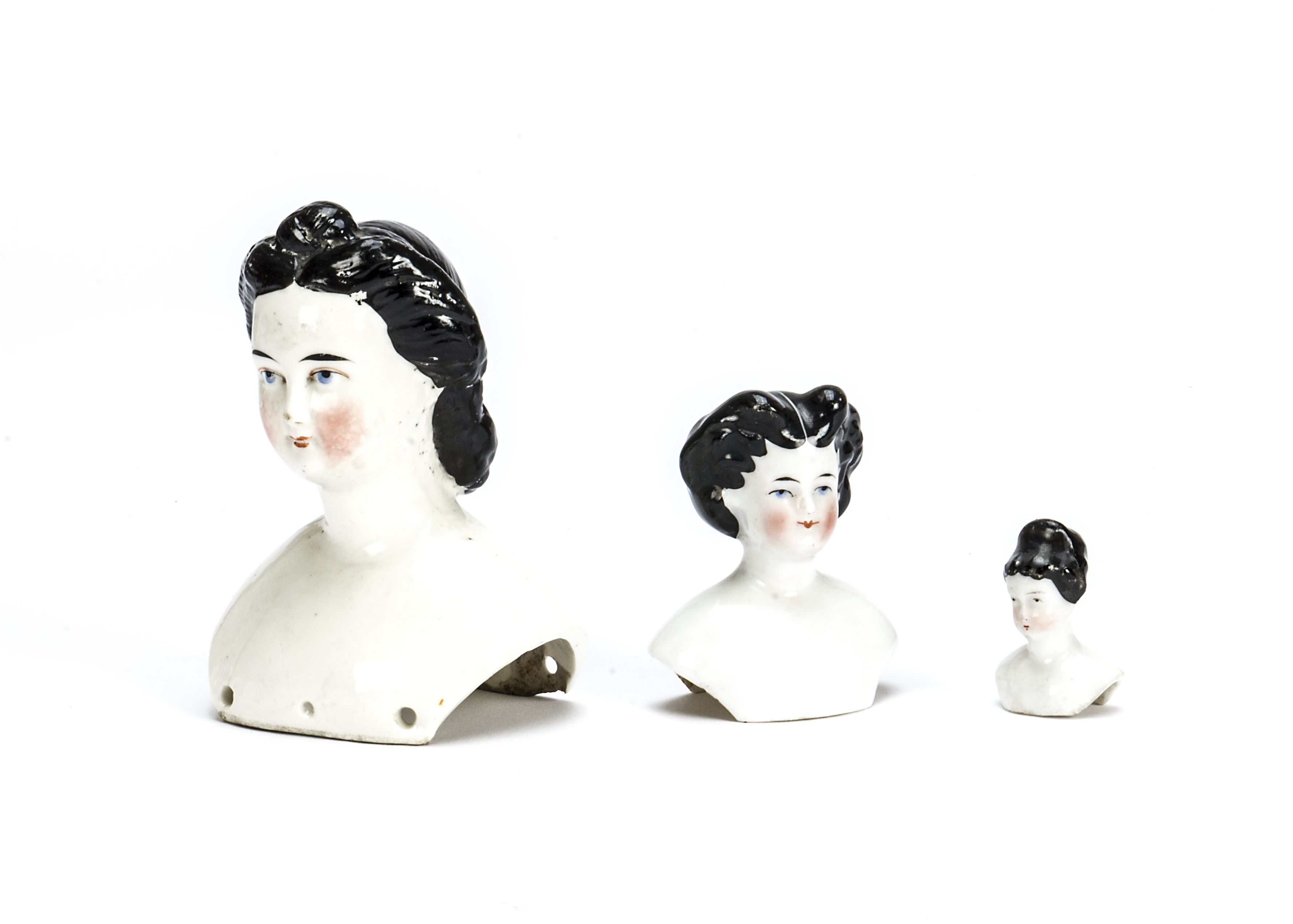 Three china shoulder head doll heads, the largest with elaborate hair rolled around hairline held in