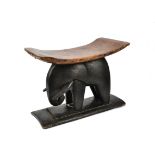 A late 19th Century wooden stool, with a curved leather covered seat, set on an elephant shaped