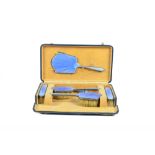 A cased six piece dressing table set, with blue enamel engine turned decoration and silver backs,