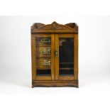 An early 20th Century oak smokers cabinet, with two bevelled glass doors revealing three drawers