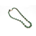 A late 19th/early 20th Century yellow metal green paste necklace, the graduated oval cut glass