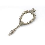 An Edwardian white metal and paste encrusted hand mirror, in floral design surmounted with a