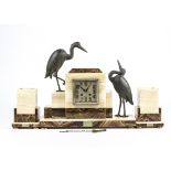 An art deco alabaster clock group with spelter mounts, the mounts in the form of herons one gazing