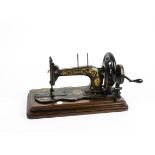 A Victorian Singer hand cranked sewing machine, attached to a hinged wooden base, 43cm x 23cm (