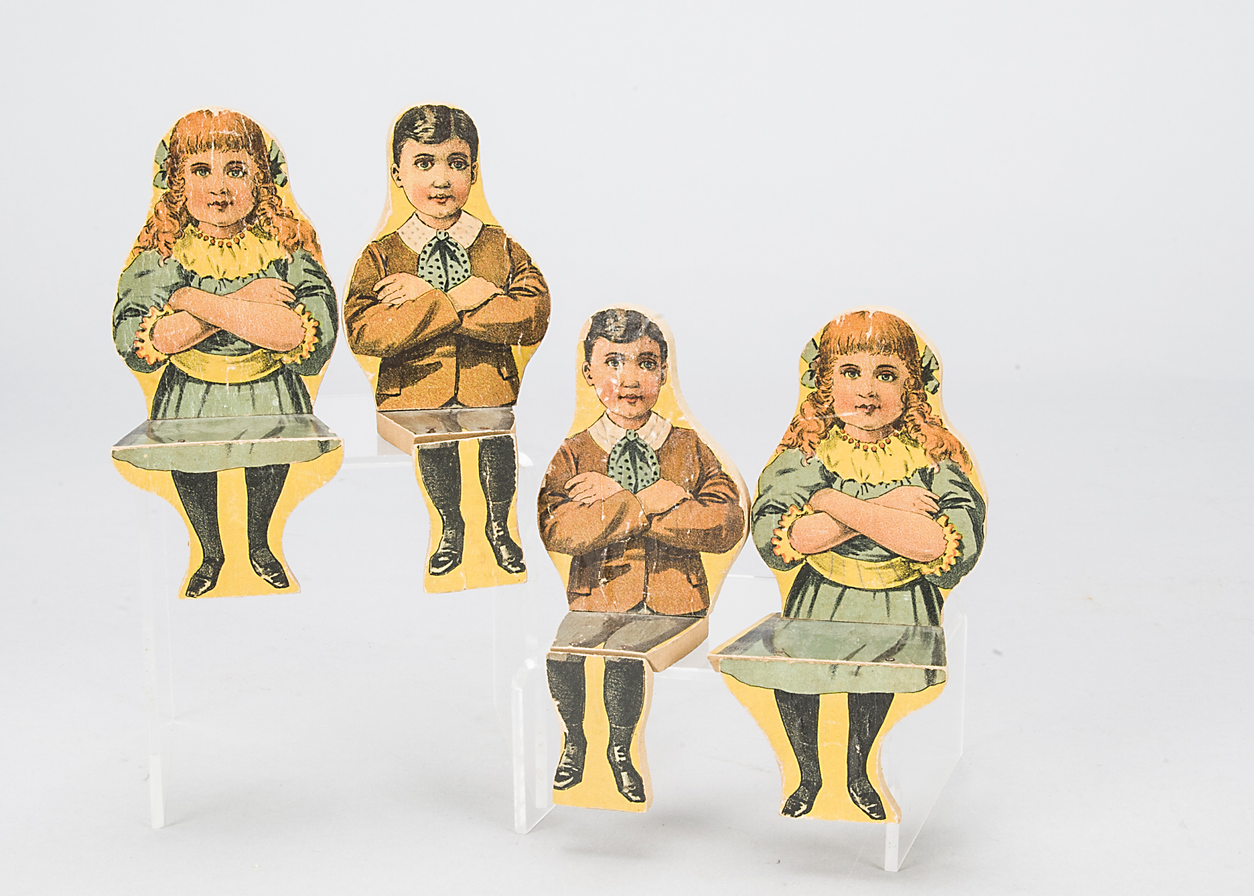 Four toy seated wooden children, printed colour paper applied to wood, two Edwardian boys and two