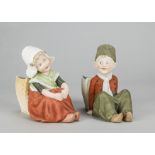A pair of Gebruder Heubach seated Dutch children, with basket posy holder, painted in red and green,
