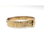 A 9ct gold bangle with floral and buckle decoratio