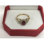 A 9ct gold ring set with a central red stone surro
