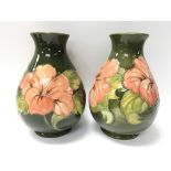 A pair of green Moorcroft vases decorated with hibiscus flowers. Measures approx 20cm tall.