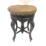 A Victorian carved wooden piano stool with revolving brown leather top studded with buttons.
