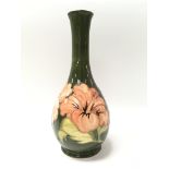 A green Moorcroft vase decorated with hibiscus flowers. Measures approx 26cm tall.
