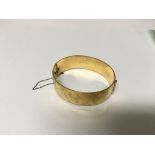 A gold tone bangle with scrolled decoration