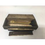 A small old wooden box containing two vintage spirit levels, five brass mounted wooden rulers and