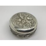 A silver box of circular shape decorated with figu