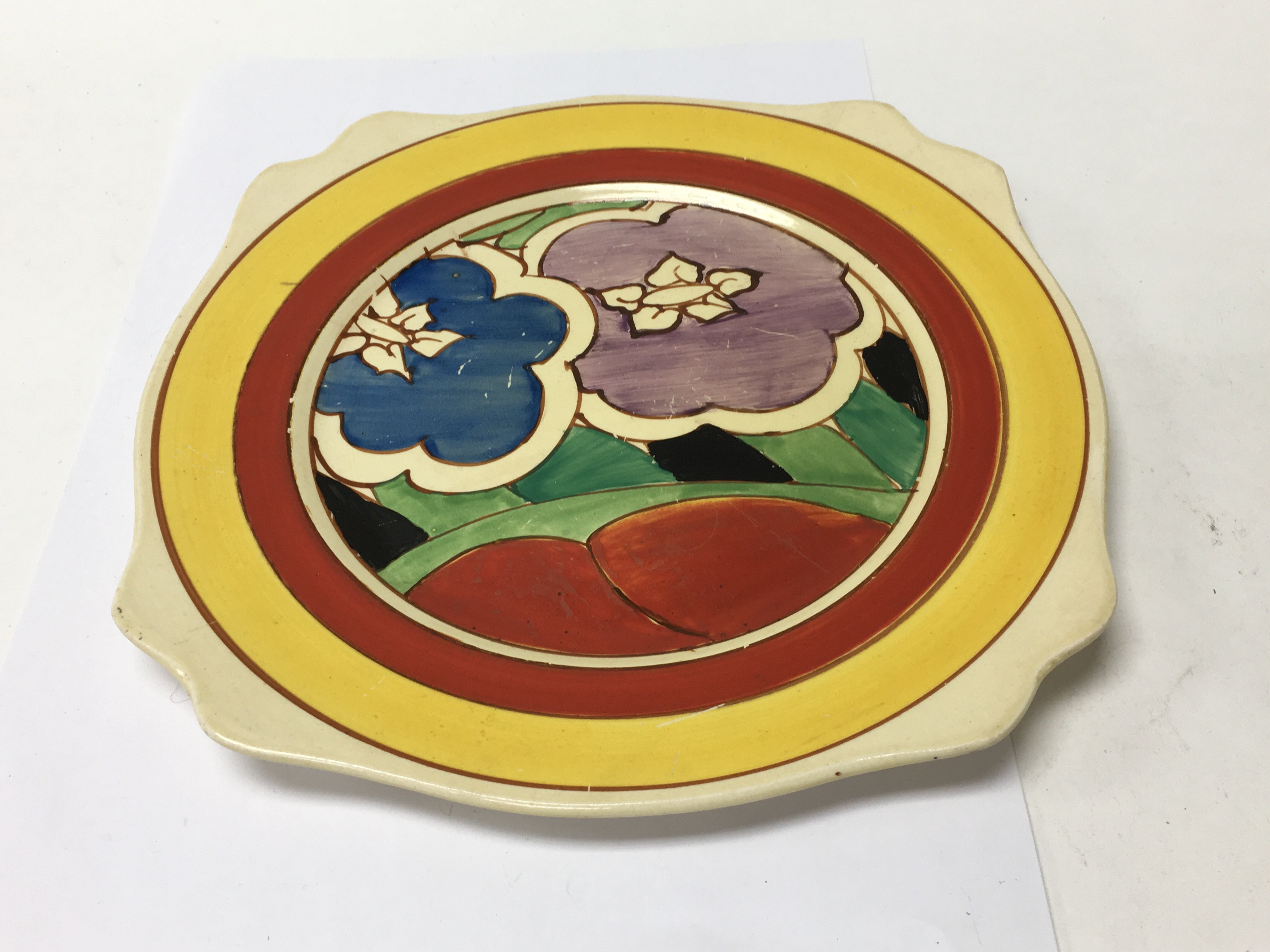 A Clarice Cliff plate decorated with flowers and f