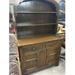 A small oak dresser with a raised back and shelves above drawers and cupboards.