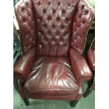 A wing back open arm chair with button back on square tapping legs .