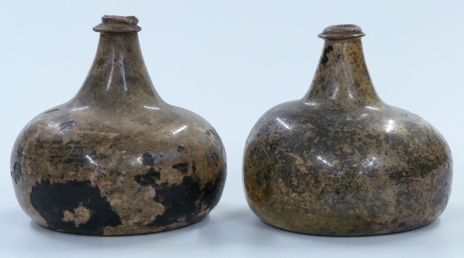 A near pair of early 18thC green glass onion wine bottles with iridescent finish, by repute dug up