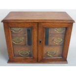 Oak desk top or similar cabinet the bevelled glazed doors opening to reveal six drawers, width 34cm