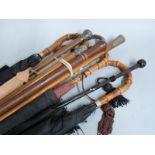A collection of walking sticks, umbrellas and parasols including two with hallmarked silver mounts/