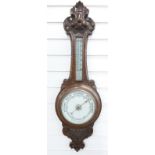 A early 20thC carved oak aneroid barometer, the white enamelled dial with bold black predictions,