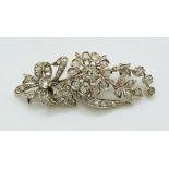 An early 20thC gold brooch set with diamonds in a floral, bow and foliate design, 6cm long