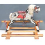A carved dapple grey rocking horse on pine base with padded saddle and leather truck, height 93cm,