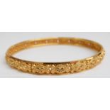 A yellow metal bangle with raised decoration marked 22ct gold, 17.6g (6.5 x 6.3cm)