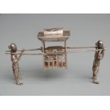 Chinese white metal novelty table ornament formed as a covered seat carried by two figures, marked