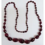 A cherry amber necklace of 65 graduated faceted oval beads, the largest 26.7x21.7mm, 68g.