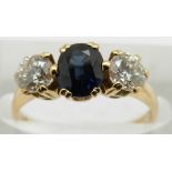 An 18ct gold ring set with an oval cut sapphire flanked by a diamond measuring approximately 0.