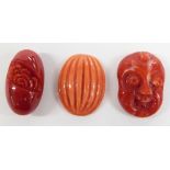 A carved coral head of a laughing man and two carved coral beads